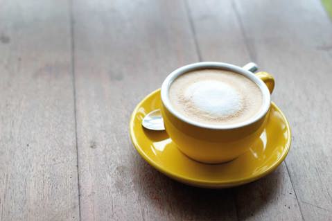A latte coffee in a yellow mug on a saucer