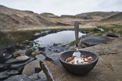 Bowl full of Arla Skyr topped with berries and granola, placed on a rock with mountains in the background