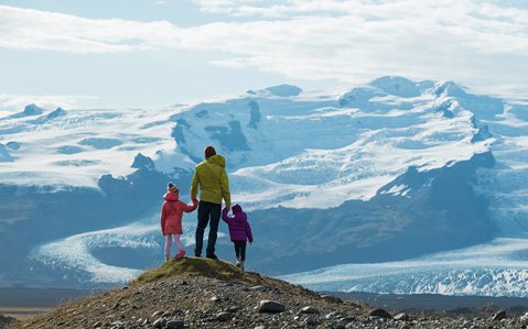 Man standing on mountain with two young children holding on either side holding his hand while looking out to the view ahead of them