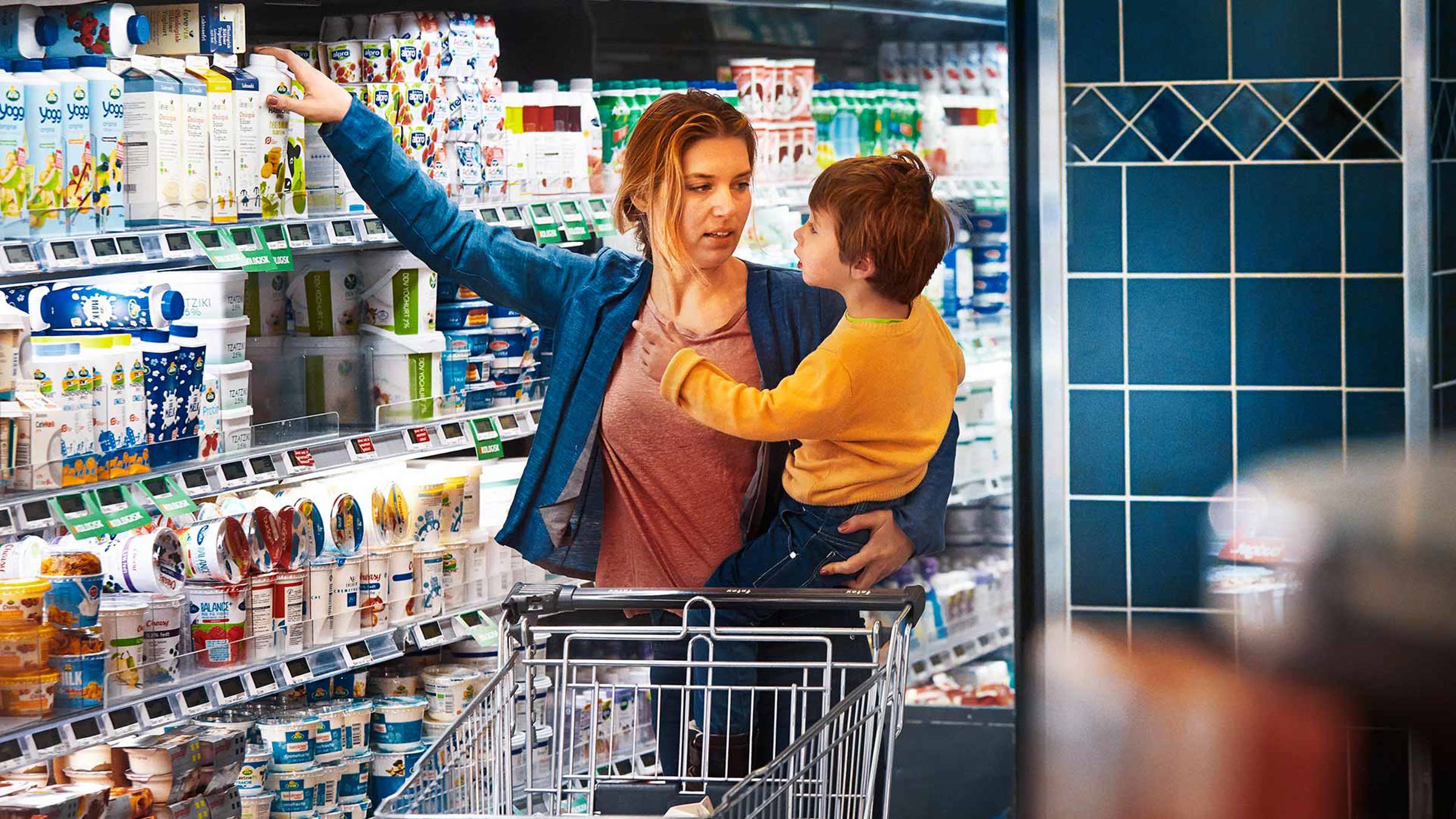 A mother holding her child and picking up a carton of Arla milk at a supermarket