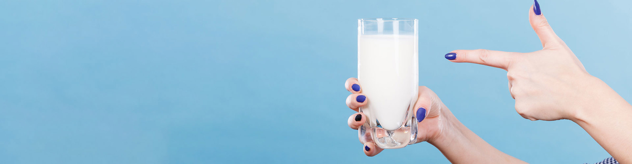 A pair of hands with purple painted nails with one hand pointing towards a glass of milk held in the other