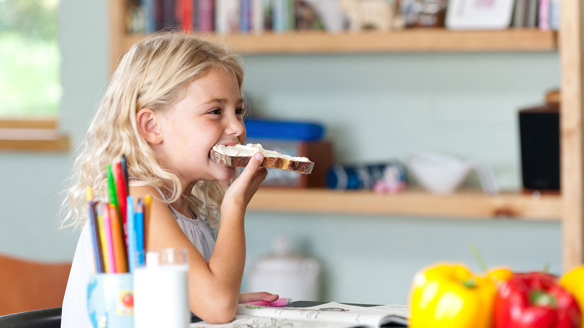 A girl eating a slice of bread with cream cheese