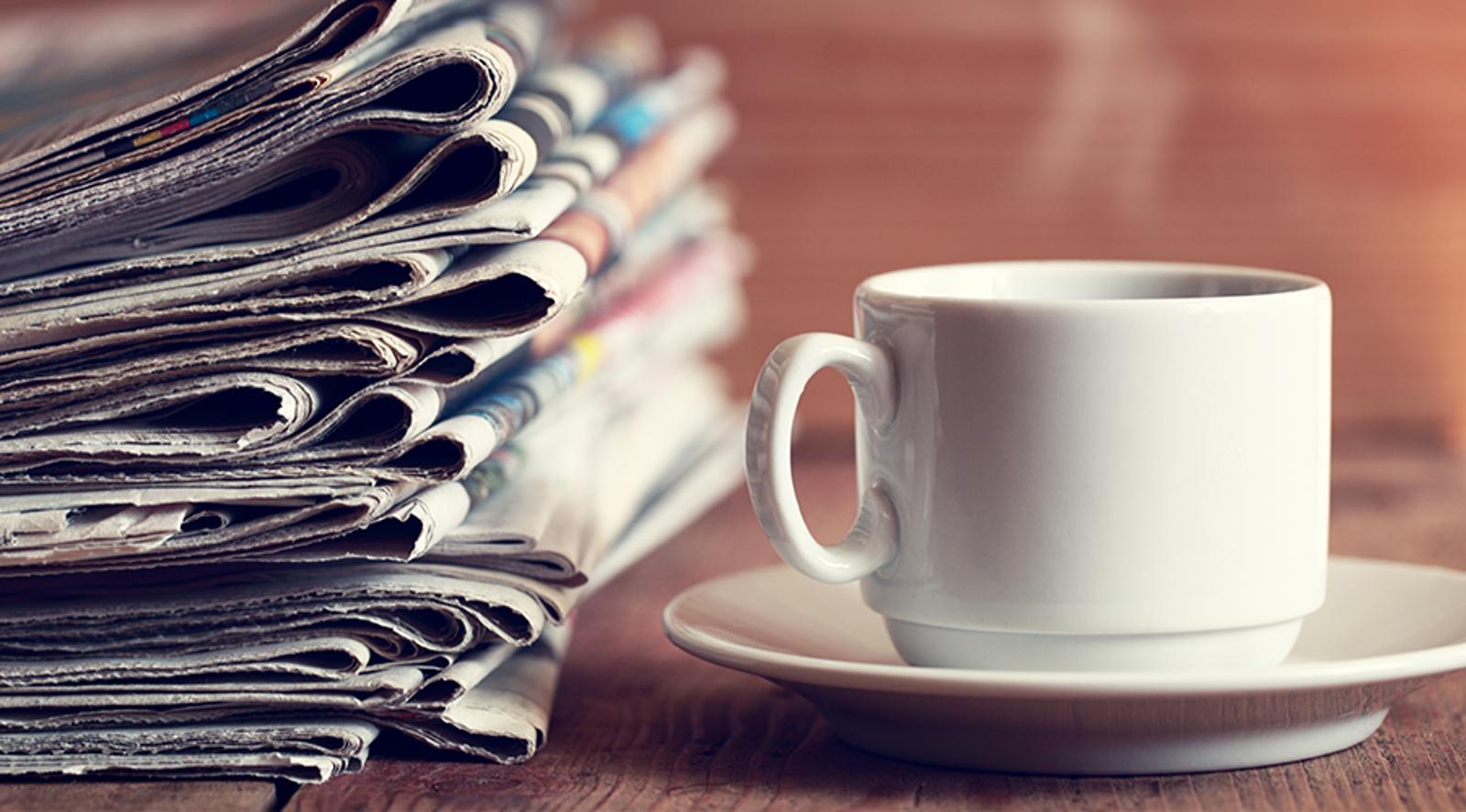 A steaming mug next to a stack of newspapers