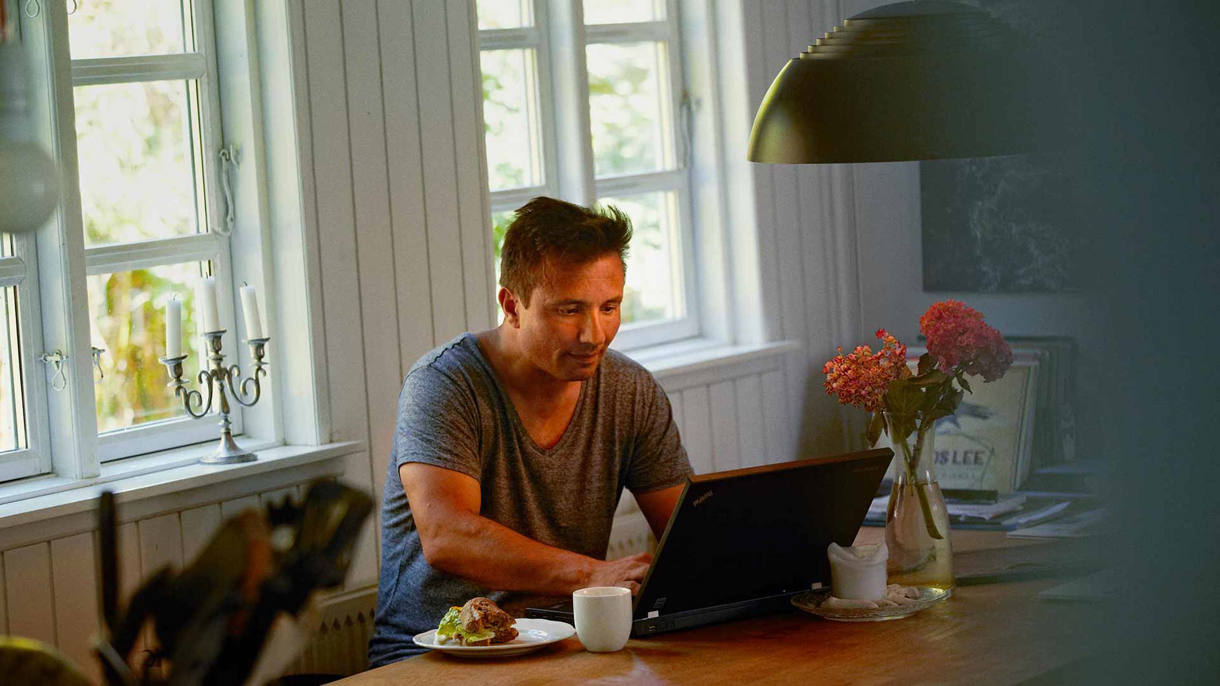 Man using a laptop with a sandwich and mug by his side