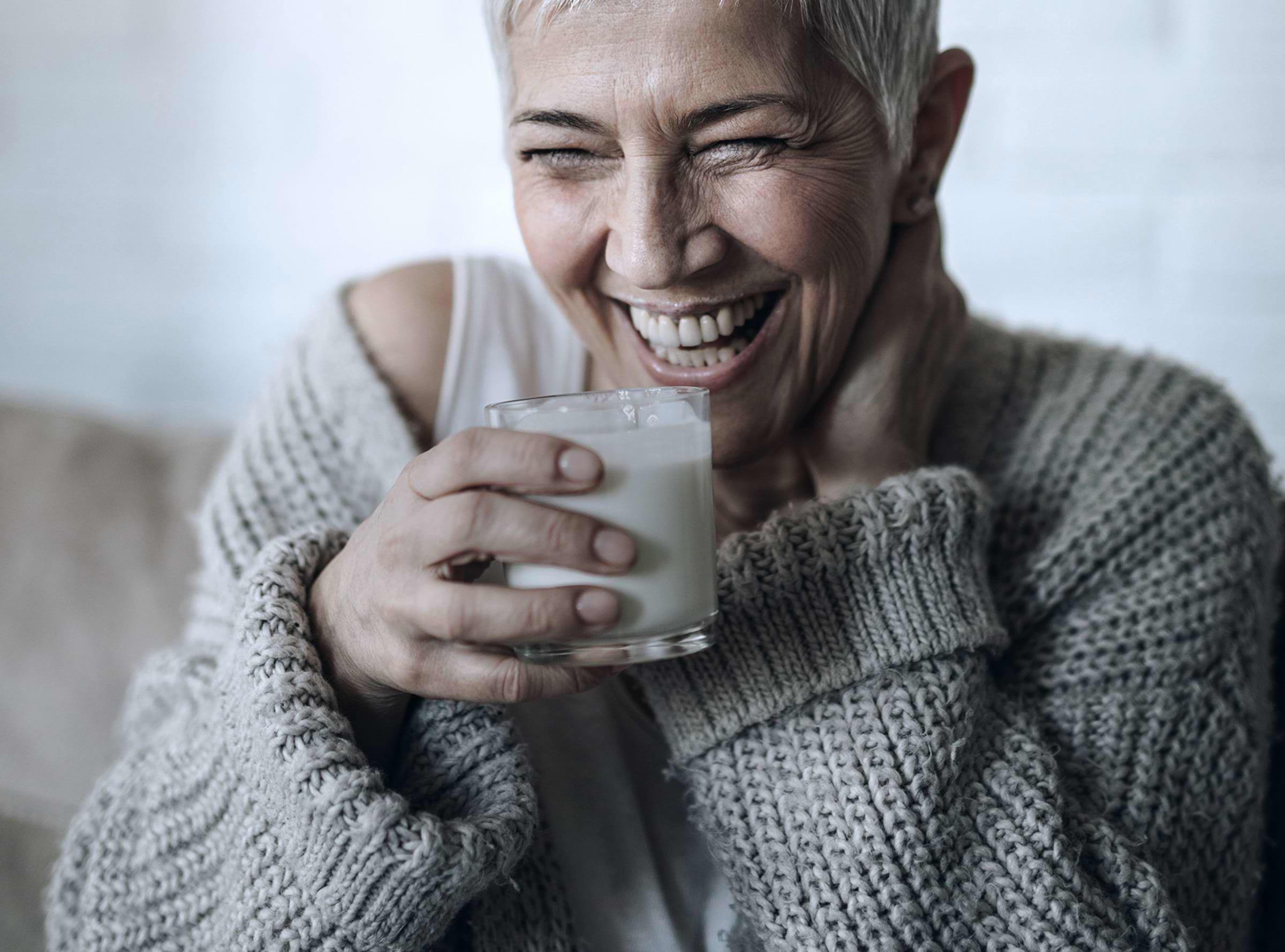 A woman laughing with a glass of milk in her hand