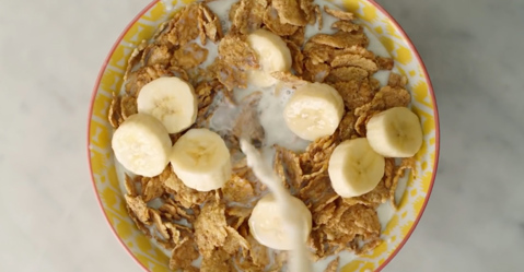 Milk being poured into a bowl of cereal with banana slices