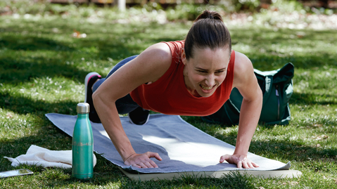 Woman in red top grimacing as she does pressups outdoors on a workout mat