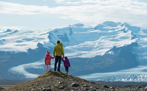 Man standing on mountain with two young children holding on either side holding his hand while looking out to the view ahead of them