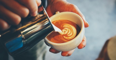 Milk jug being poured into a cup full of espresso