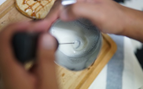 A milk frother being used in a milk jug