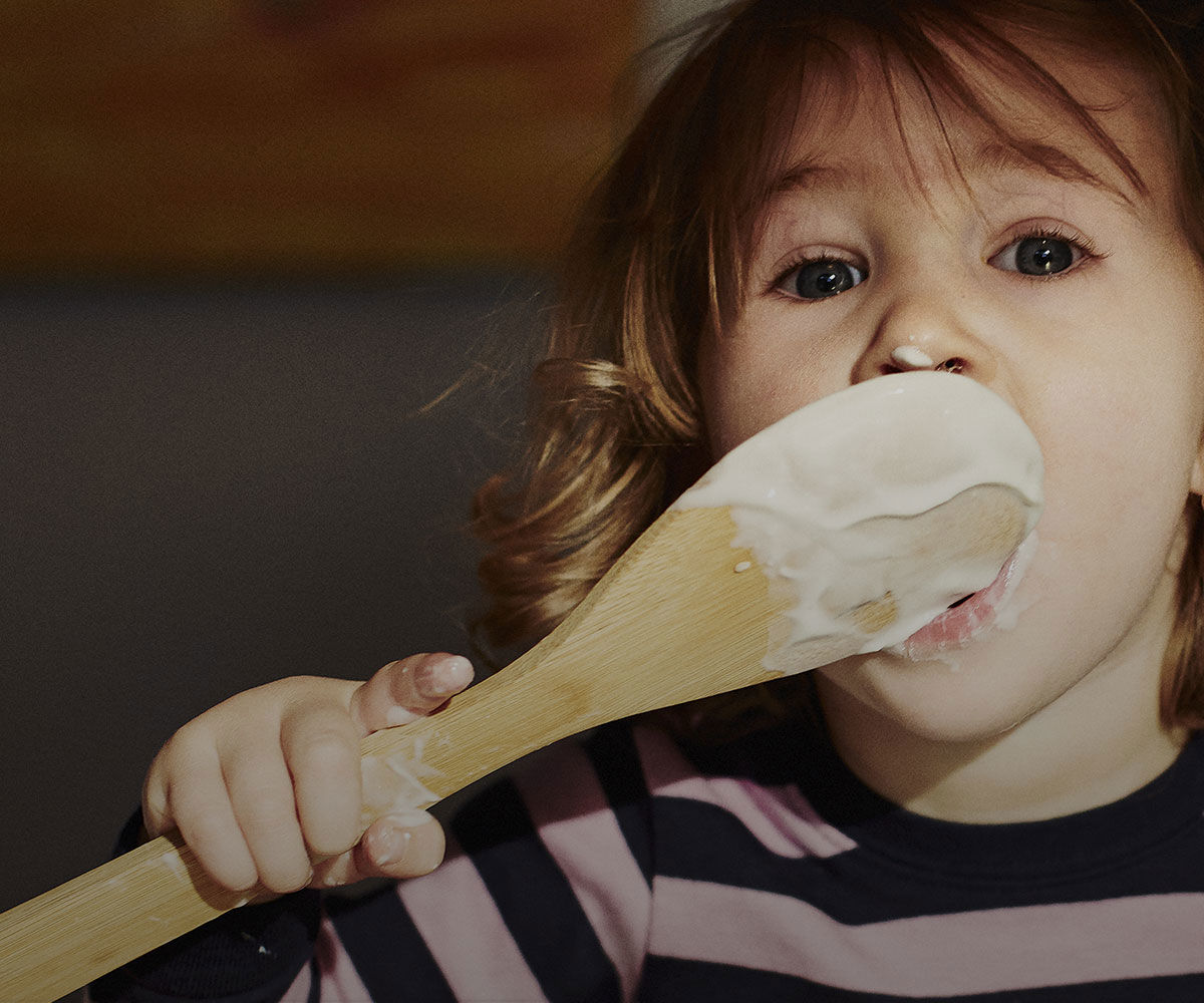 Child licking a cream covered wooden spoon
