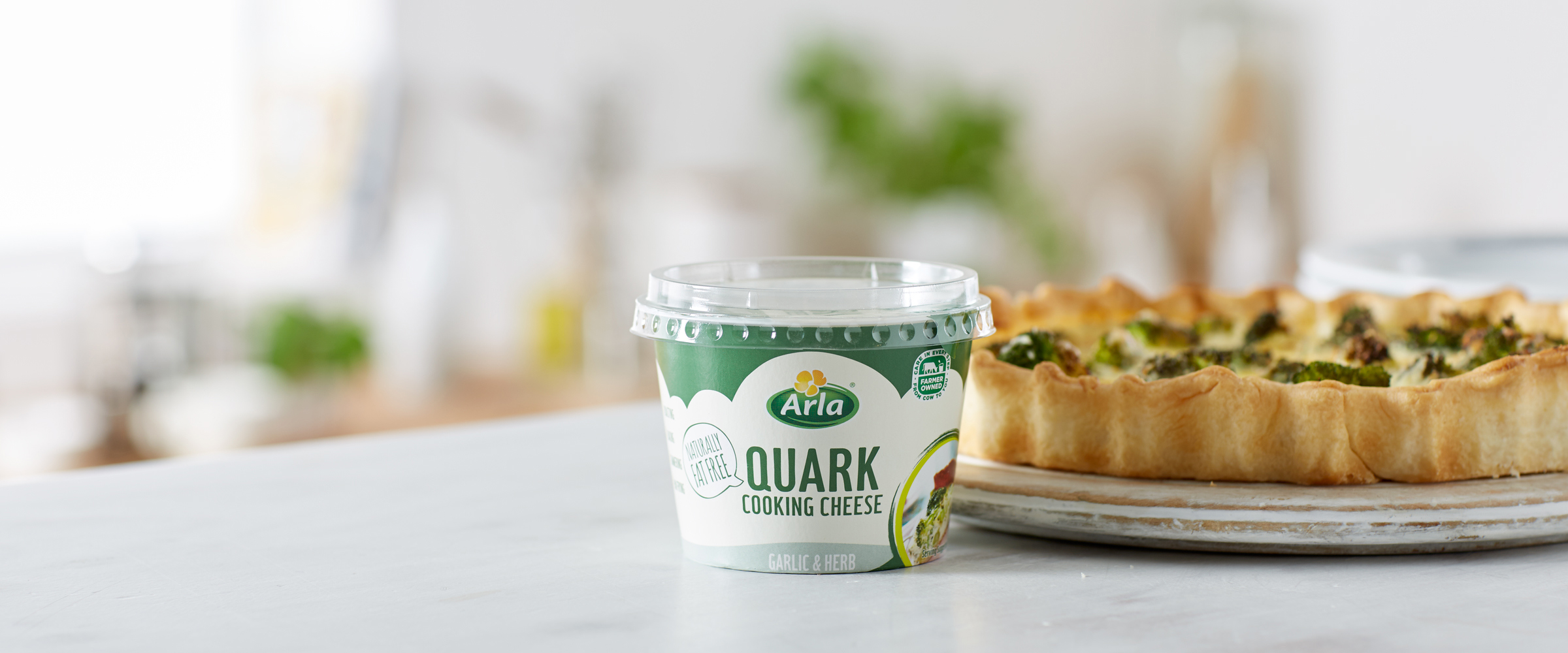 A tub of Arla Quark Garlic & Herb in front of a broccoli quiche