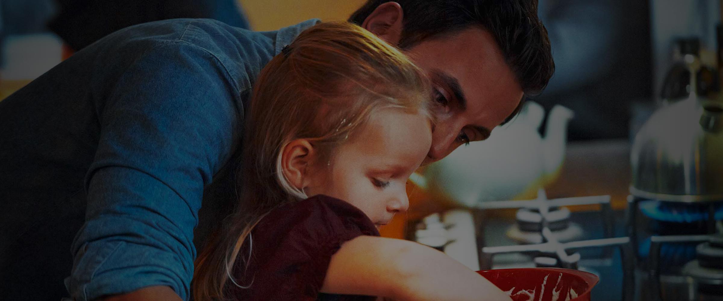 A child at a stove being hugged by her father