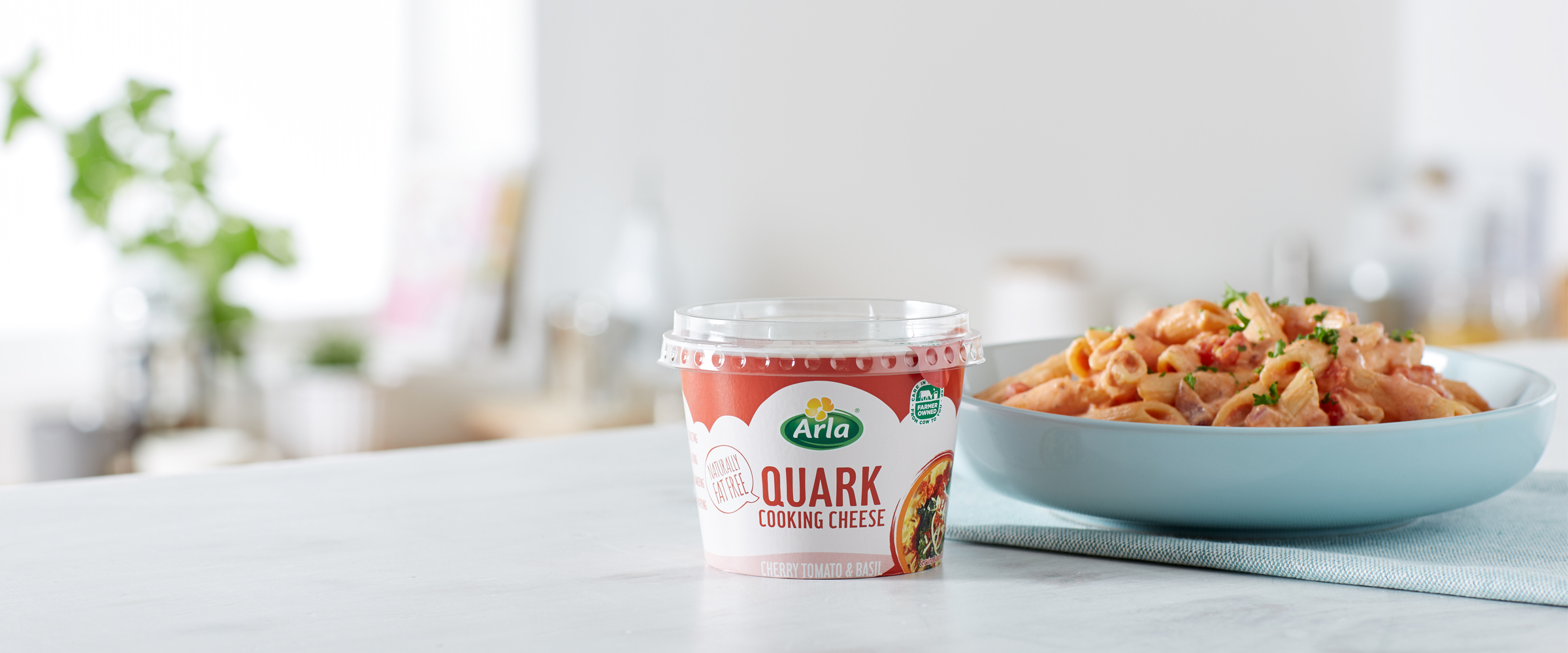 A tub of Arla Quark Cherry Tomato & Basil in front of a pasta dish