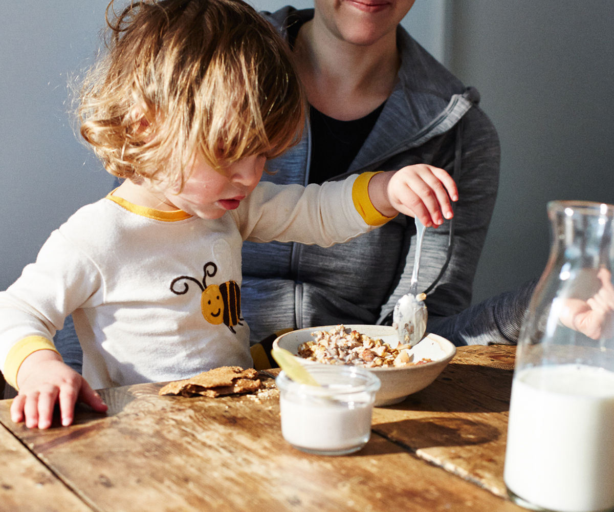 A young child on their mothers lap eating oats