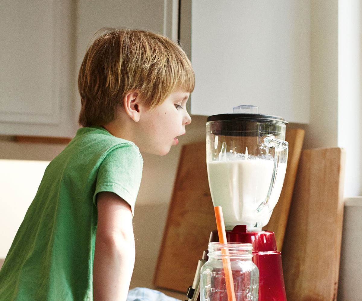 A young child watching a milk drink in a blender