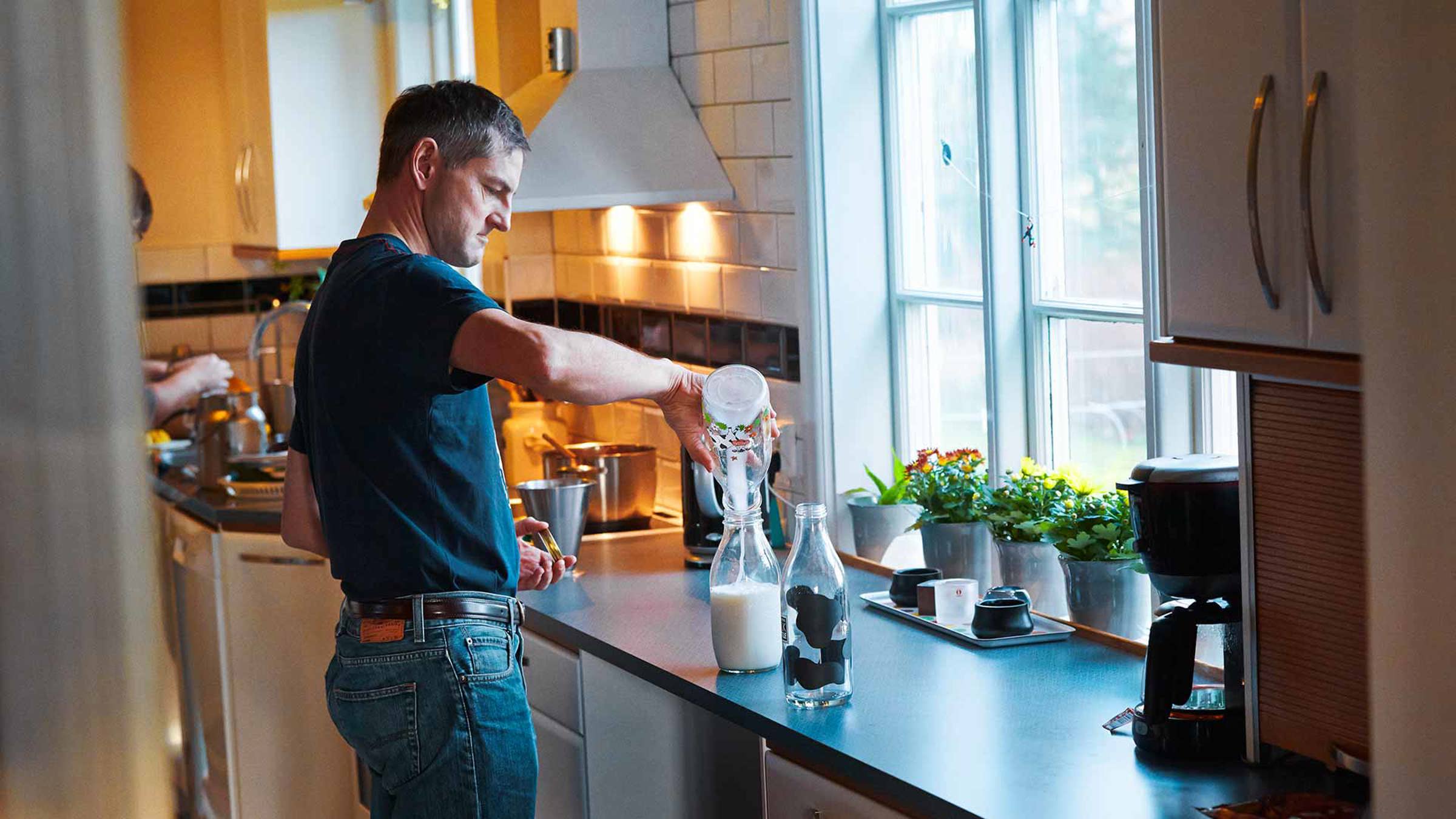 A man decanting milk into a jar in a kitchen