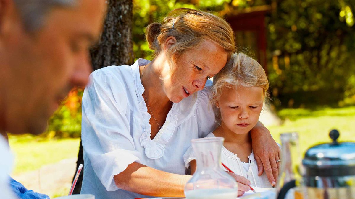 A mother and her child writing at a table outside