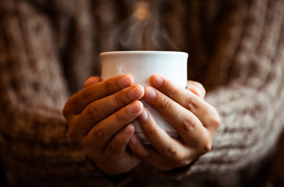 A pair of hands holding a steaming mug