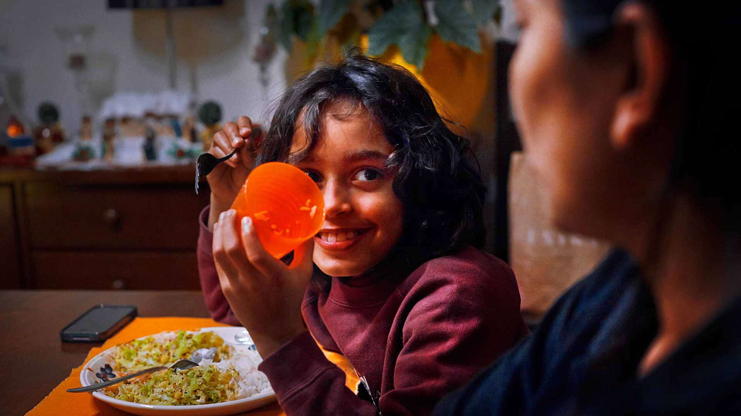 A child showing a cup to their mother over dinner
