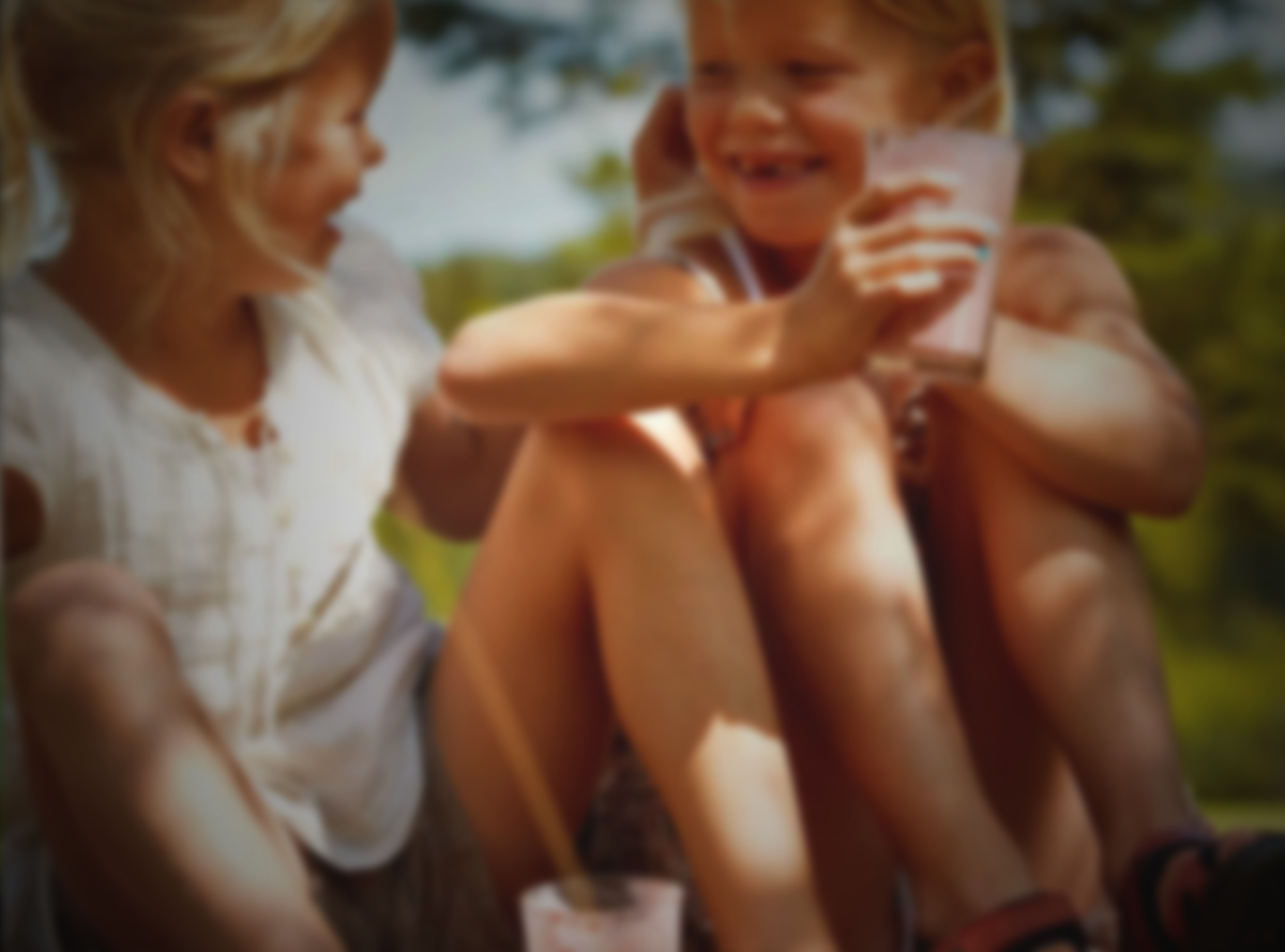 Two children sat down outside drinking milk