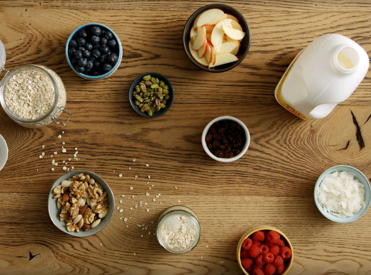 Ingredients for overnight oats: oats, apple slices, walnuts, pistachio nuts, coconut flakes, berries, raisins and milk