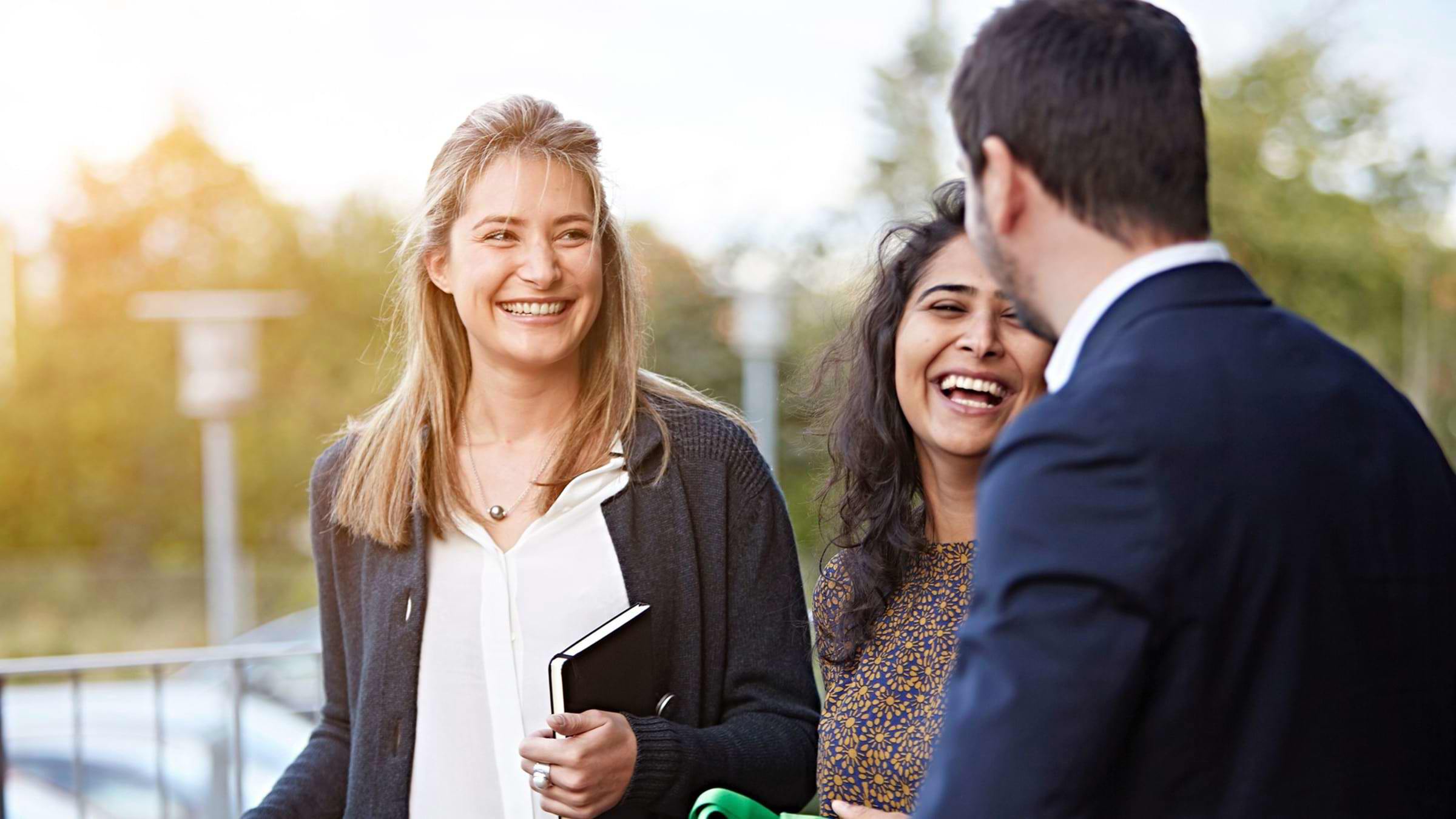 Two women laughing with a man outside