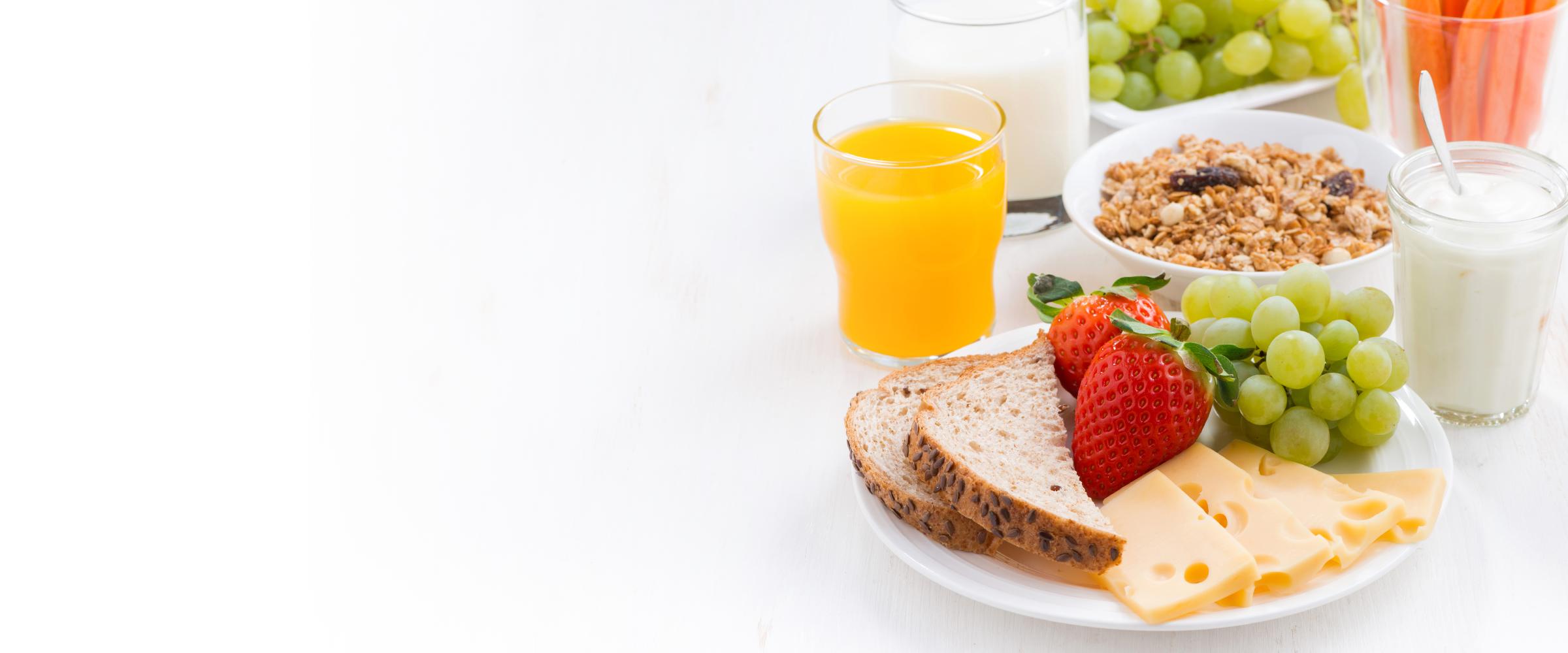 A breakfast of bread, cheese, grapes, strawberries, yoghurt, oats and orange juice