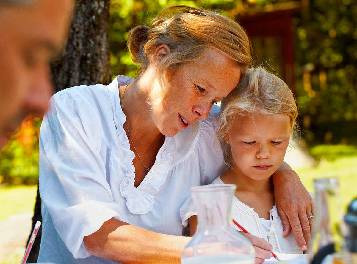 A mother writing with her child at an outside table