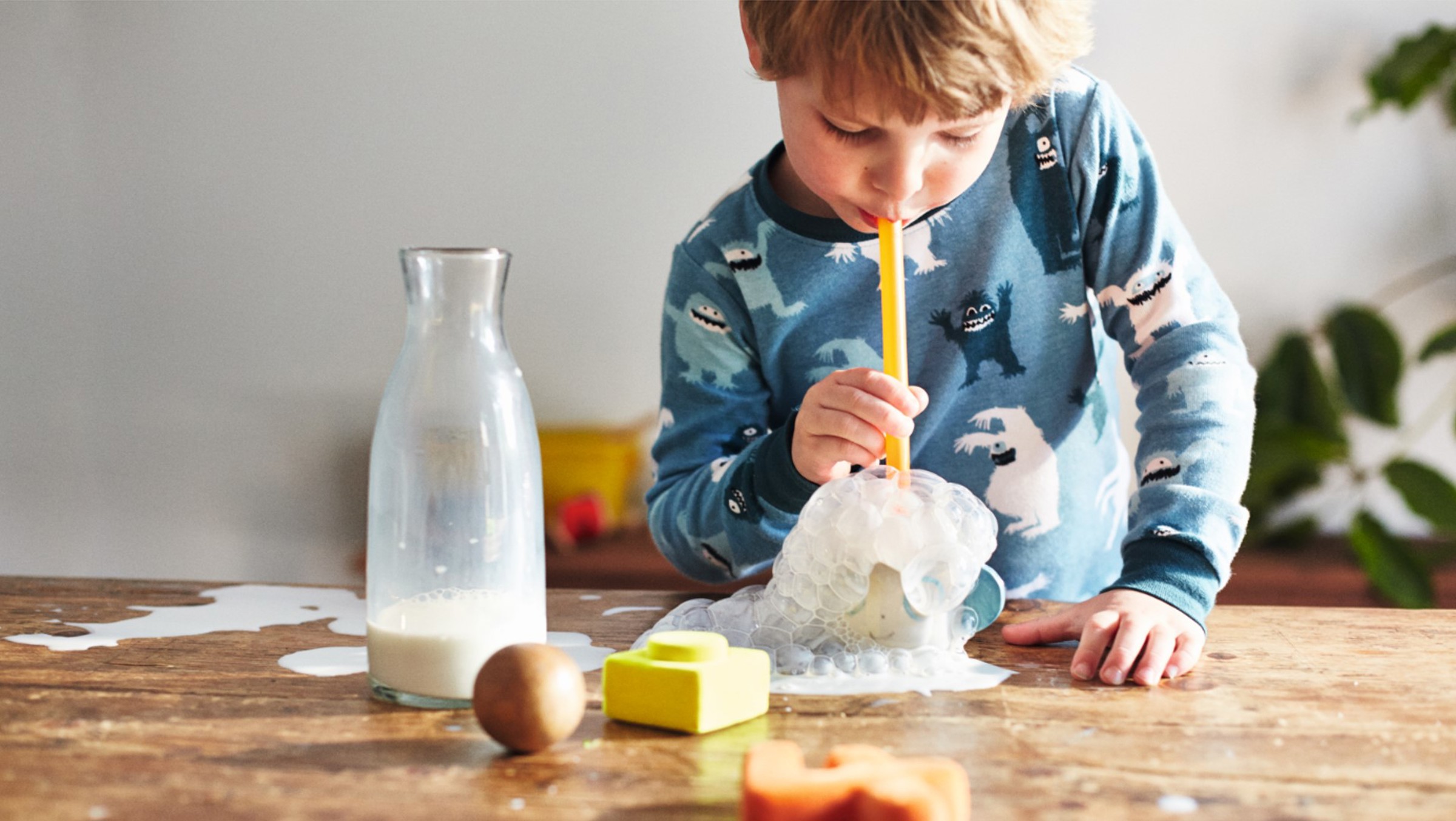 A small boy blowing bubbles through a straw into a cup of milk 