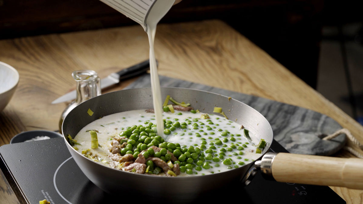 Milk being poured over thai green curry ingredients in a wok