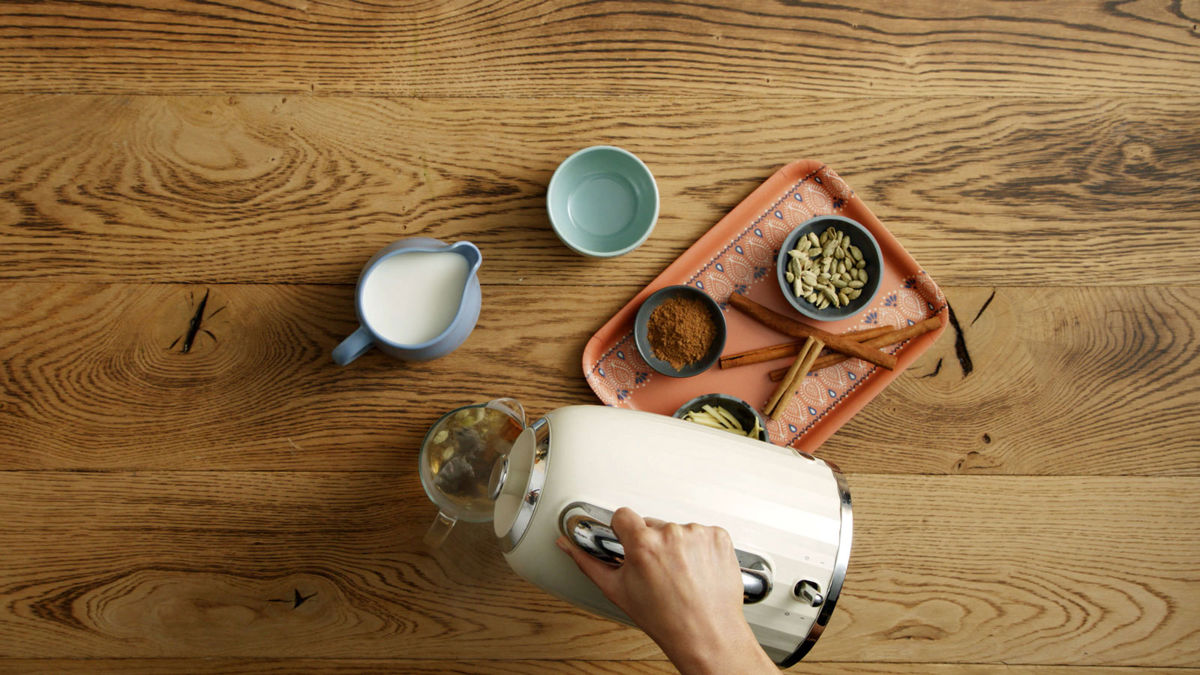 A kettle being emptied into a glass jar of chai latte ingredients