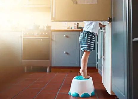 A child standing on a stool to look inside a fridge