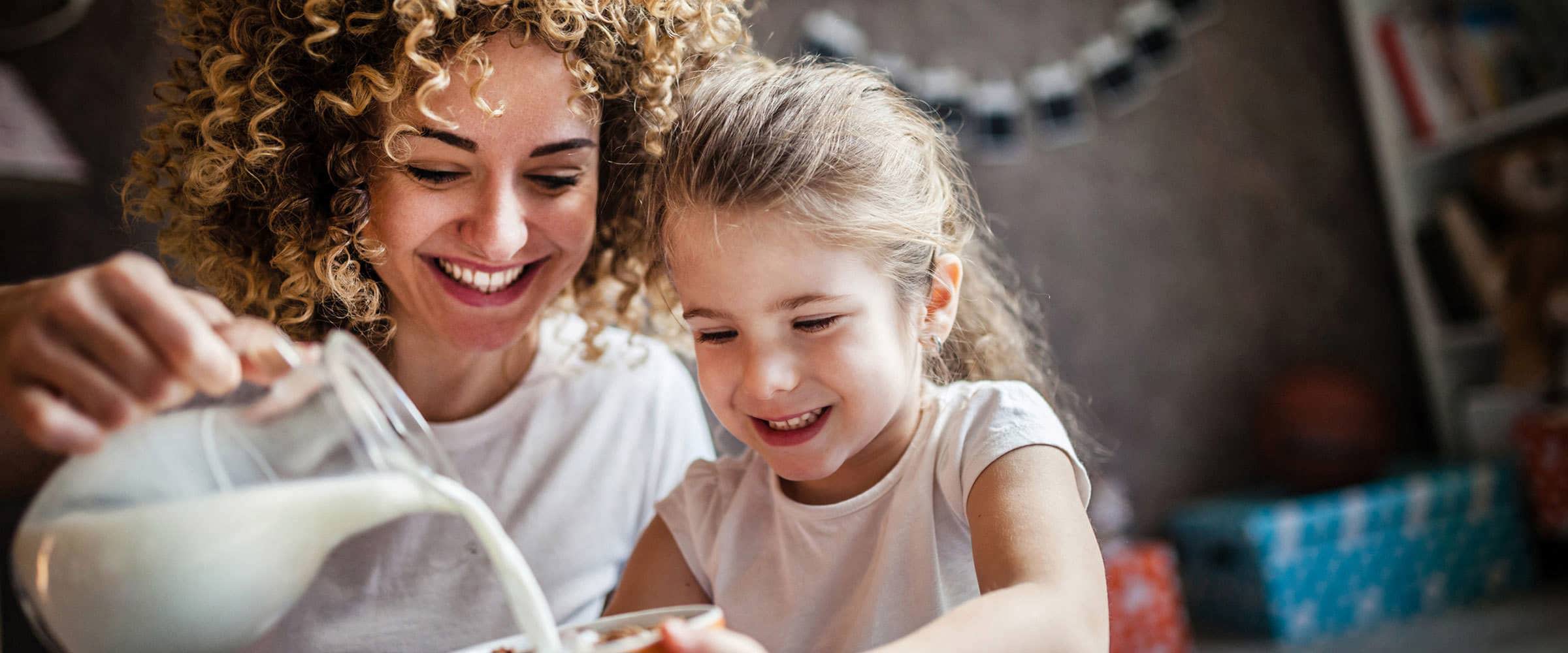 A mother pouring milk into her daughters bowl