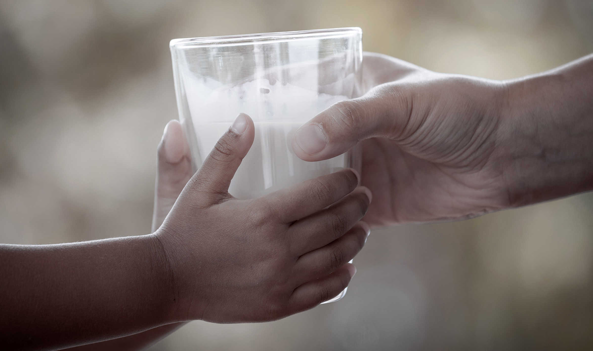 the hands of a child receiving a glass of milk from an adults hand